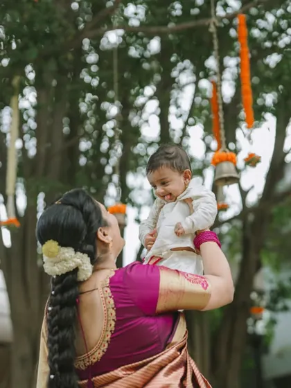 A mother's happiness shines as she lifts her smiling baby. This candid shot, taken during a naming ceremony, is full of the natural joy that makes these events so special.