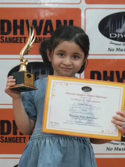 A very young student proudly holds her certificate and trophy.