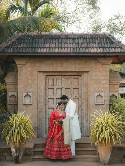 A regal portrait of the couple standing before a grand, traditional stone gateway, their foreheads touching in a moment of quiet connection.