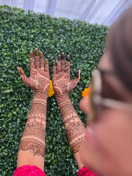An over-the-shoulder view of a bride's full mehendi, showing the beautiful flow of the design from her palms to her forearms.