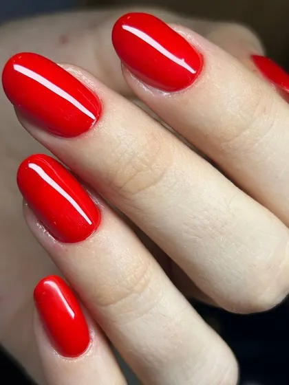 A classic, bright red manicure on oval nails. The color is vibrant and the application is perfectly smooth, showcasing a timeless look.