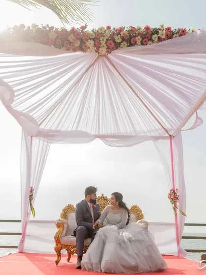 A wide shot showing the couple's engagement setup by the sea. The mandap, the ocean, and the sky create a beautiful, scenic environmental portrait.