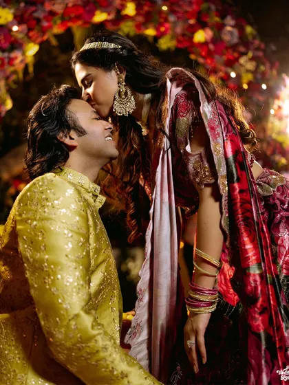 A romantic portrait of the bride kissing the groom's forehead under a stunning floral archway.