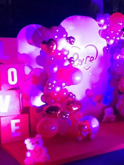 A "LOVE" themed stage illuminated with purple and red lights, featuring light-up letter blocks and heart-shaped foil balloons for a dramatic and romantic effect.