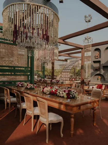 A long table setup for a grand feast. The combination of floral runners, elegant chairs, and overhead chandeliers creates a sophisticated and inviting dining experience.