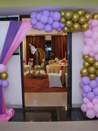 The entrance to a butterfly-themed party, featuring a balloon arch with purple, pink, and gold balloons.