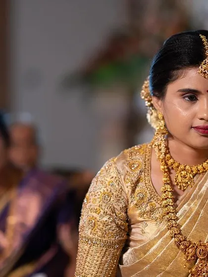 A candid shot of the bride during her wedding ceremony. The makeup remains fresh and radiant, with a focus on defined eyes and a soft lip color that complements her gold jewellery.