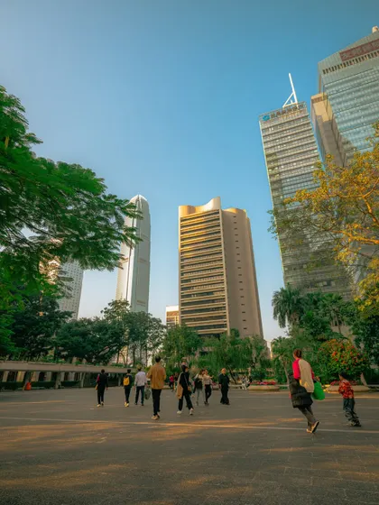 People enjoying the golden hour glow in a Hong Kong park, with the city's skyscrapers towering in the background. It's a perfect blend of urban life and natural beauty.