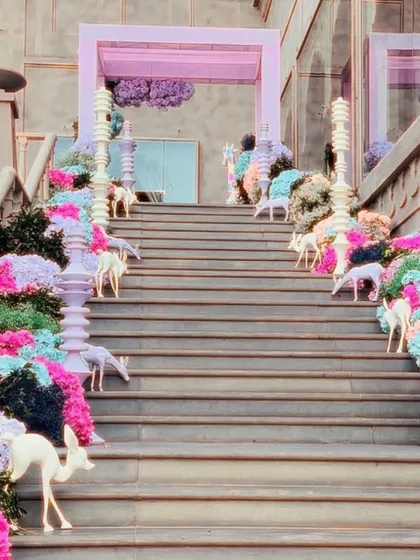 A grand staircase decorated for a whimsical carnival-themed wedding, with colorful flowers and small deer props lining the steps.