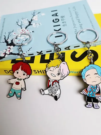 A styled shot of the BTS metal keychains, showing the high-quality finish and vibrant colors of the J-Hope, Jimin, and RM designs.