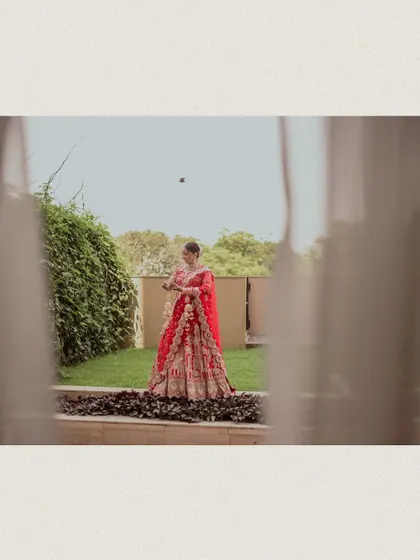 A creatively framed shot of the bride in the garden, seen from inside through a window.