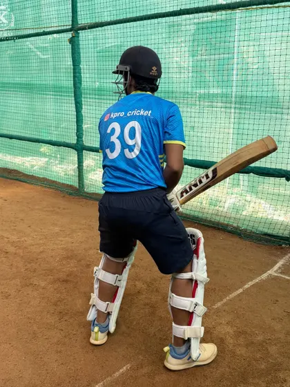 A young cricketer in full gear, ready to face bowlers in the outdoor nets. The focus is on building confidence and technique on a clay surface.