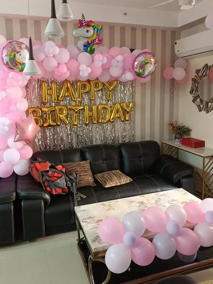 A pink unicorn-themed birthday decoration for a living room. This setup includes a balloon arch over the sofa and a unicorn foil balloon.