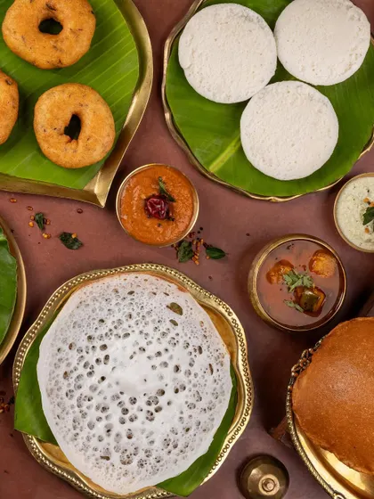 A beautiful flat lay of a South Indian breakfast spread, including appam, vada, and idli, served on traditional banana leaves.