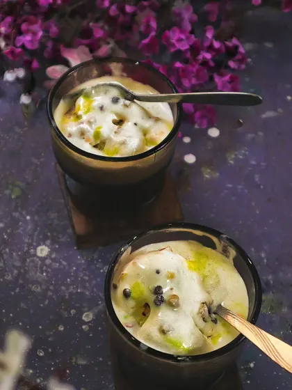 Two glasses of pistachio ice cream, shot from above in a dark and moody style. The purple flowers in the background add a pop of color and an element of elegance.