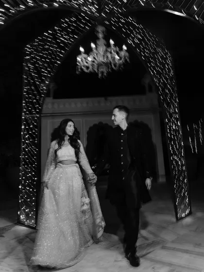 A classic black and white photograph of the couple walking hand-in-hand through a beautifully lit archway. This image showcases our artistic approach, creating a timeless and romantic memory of their journey together.
