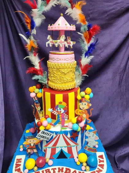 A grand 3-tier carnival cake with a rotating carousel on top. This masterpiece is surrounded by feathers and features clowns, monkeys, and balloons, creating a spectacular centerpiece for a birthday carnival.