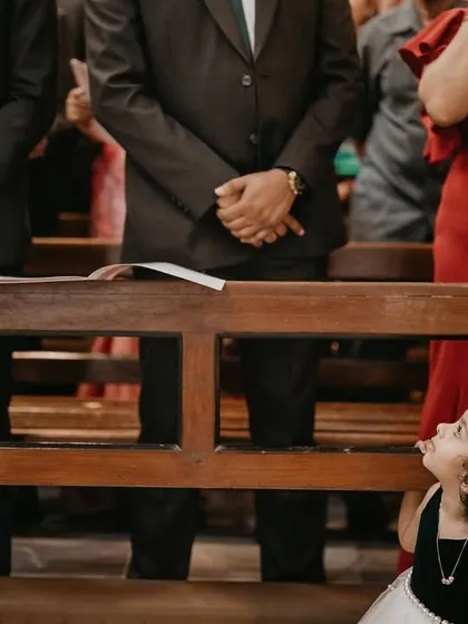 A little girl with curly hair peeks playfully from under a church pew. This image is a perfect example of capturing the spontaneous and cheeky moments that make child photography so delightful.