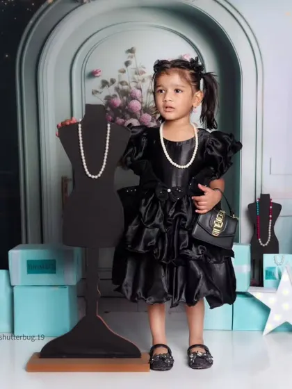 A toddler striking a pose in a beautiful black dress, surrounded by shopping bags in our high-fashion theme.