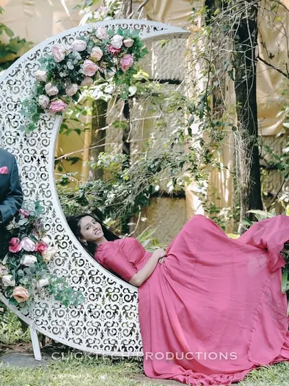 A creative pre-wedding photo with the bride lounging on a floral crescent moon prop. This kind of stylized shot adds a fairy-tale element to your photo album.