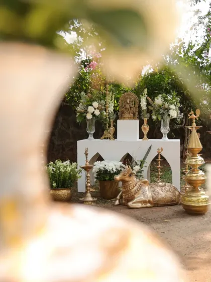A sacred corner setup, featuring a Ganesha idol, a Nandi statue, and various brass lamps, all adorned with white flowers for a serene and spiritual feel.