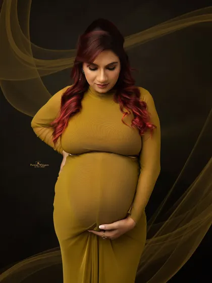 A quiet and contemplative solo portrait. The mother-to-be looks down at her baby bump, her hands gently cradling it in a classic gesture of maternal love.