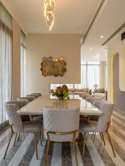 A front-on view of the dining table, highlighting the quilted chairs and the hexagonal mirror art on the wall. The design is a perfect balance of texture, reflection, and minimalist elegance.