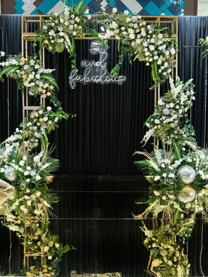 The full view of the black and gold 50th birthday photo booth. The floral arch, neon sign, and shimmering disco balls came together to create a glamorous and fun spot for guests to capture memories.