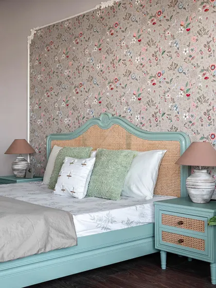 Another view of the vintage-inspired bedroom, showing the matching bedside table with rattan drawer fronts. The table lamps provide warm, ambient light perfect for evening reading.