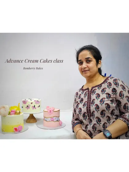A student showcasing the beautiful cakes she created in my Advanced Cream Cakes class. Each design focuses on a different skill, from piping to painting and modern decorating styles.
