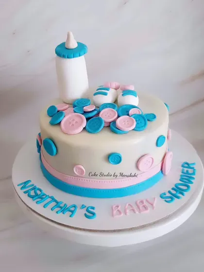 A cute baby shower cake for Nishtha. The design is decorated with pink and blue buttons, baby shoes, and a feeding bottle.