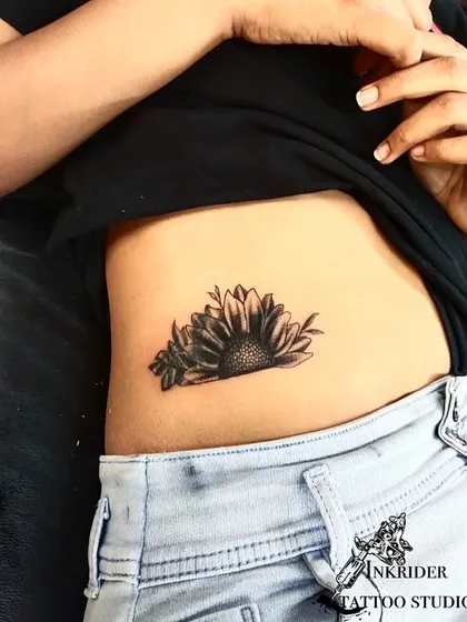 After: A black and grey sunflower design was used to cover the old tattoo. The placement and shading of the flower completely hide the name, transforming the area with a popular and positive floral design.