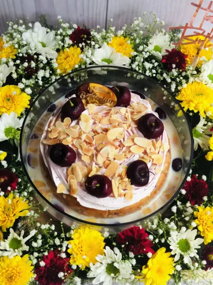 An overhead shot of the Cherry Almond Tres Leches, showcasing the beautiful arrangement of cherries and almonds on top, surrounded by a ring of colorful flowers.