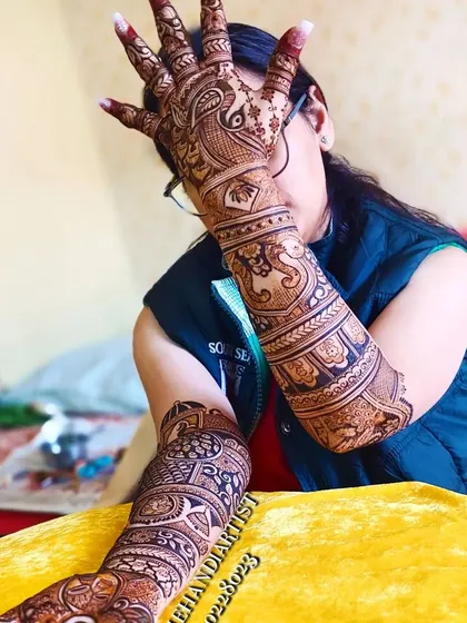 A full view of a bride's elaborate henna. This design covers both arms completely with a variety of traditional Indian wedding motifs, including peacocks and architectural elements.