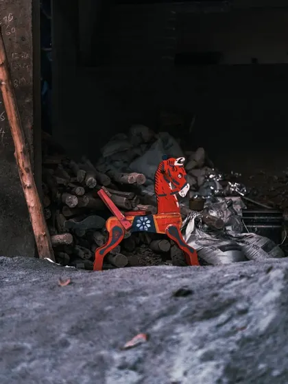 A lone, red wooden rocking horse stands out against the grey, dusty backdrop of a construction site. This image evokes a sense of nostalgia and forgotten childhood memories.