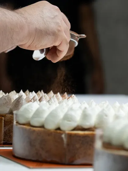 A chef dusting a tiramisu inspired cake with cocoa powder. This simple finishing touch adds a professional look and a layer of flavor.