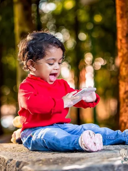 A candid shot of a toddler sitting on a stone bench in a park, completely fascinated by a phone. It's a real, unposed moment that captures modern childhood.