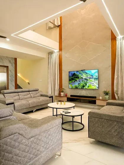 The living area in this villa features a double-height TV wall with marble finish, drawing the eye upward and emphasizing the home's spacious and airy design, complemented by comfortable, modern seating.