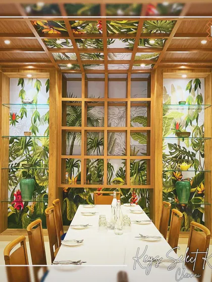 This feature wall at Keys Cafe in Chennai brings the outdoors in. A custom tropical wallpaper behind a wooden grid structure creates a stunning focal point for the main dining table.