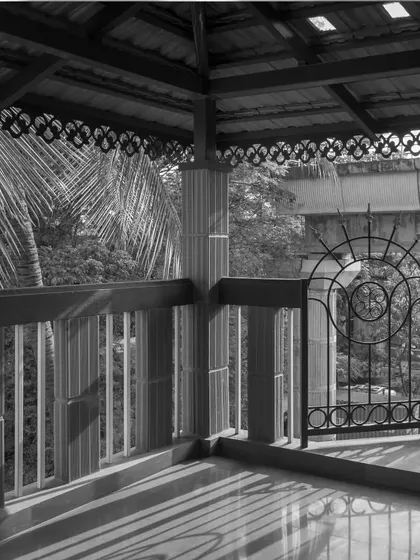 A black and white shot of a balcony, emphasizing the intricate patterns of the traditional railing and the connection to the lush greenery outside.