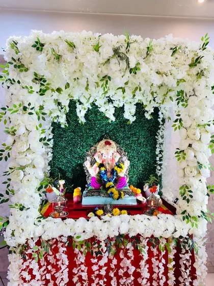 A pure and pristine Ganpati mandap made entirely of white flowers against a green grass wall. This design is perfect for creating a serene and peaceful environment for your prayers.