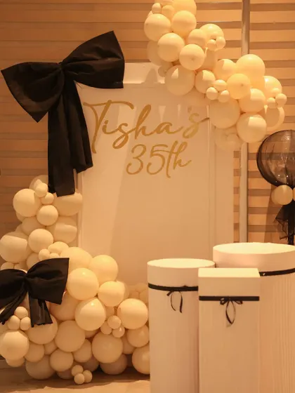 A closer look at the bow-themed 35th birthday backdrop. The design features an organic garland of cream balloons, large black bows, and personalized gold lettering.