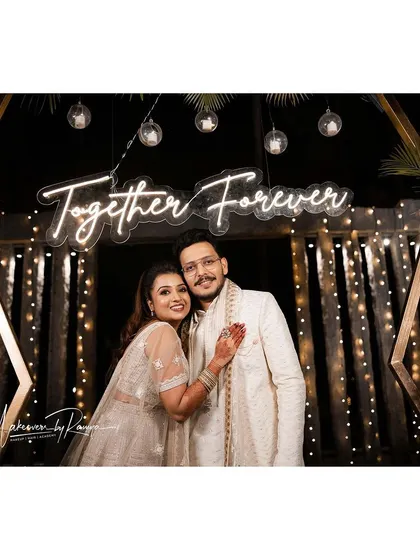 The couple posing under a 'Together Forever' neon sign, a perfect backdrop for a Sangeet night.