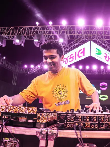 At the console during a Navratri event, with the stage lights and the massive crowd creating an electric atmosphere.
