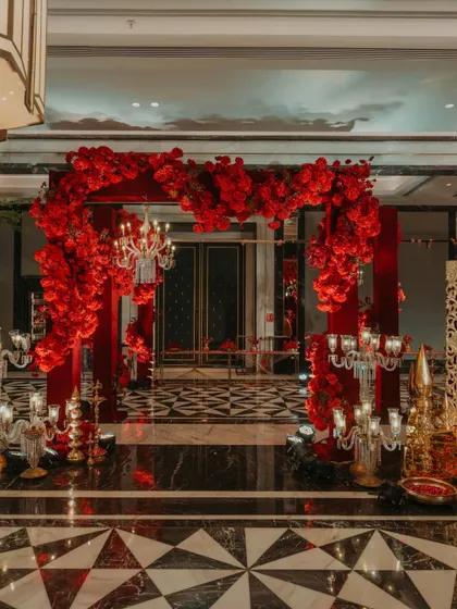 A dramatic entrance arch made entirely of lush, deep-red flowers, flanked by crystal candelabras, creating a luxurious and romantic welcome for a reception.