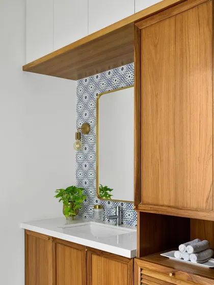 We created this chic basin niche with patterned blue tiles, a brass-framed mirror, and integrated storage for laundry and essentials.