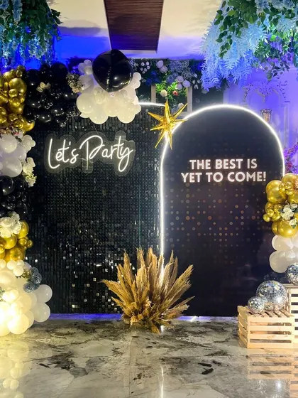 The full setup for the retirement party, with the theme "The Best Is Yet To Come." A black sequin wall, a custom arched backdrop, and a black, gold, and white balloon arrangement set the stage for a new chapter.