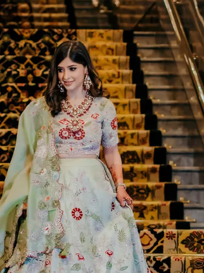 A candid shot of the bride walking down the stairs, her smile lighting up the frame. This image captures a natural, happy moment during her engagement festivities.