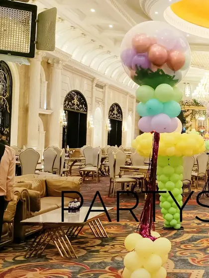 Tall, colorful balloon sculptures designed to look like candy trees, lining the aisle of the party venue.