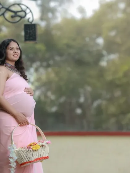 An outdoor shot with a flower basket prop, adding a touch of rustic charm to this pink saree maternity portrait.
